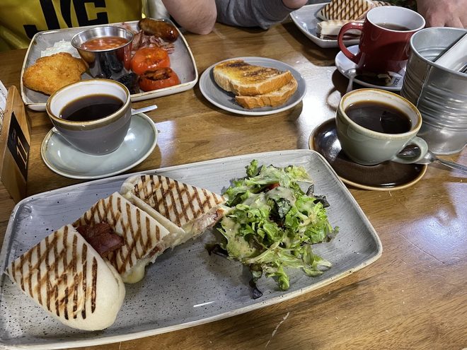 A table laid with panini, breakfast tray, toast and two black coffees
